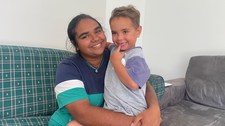 A woman sitting on a couch and smiling while hugging her son.