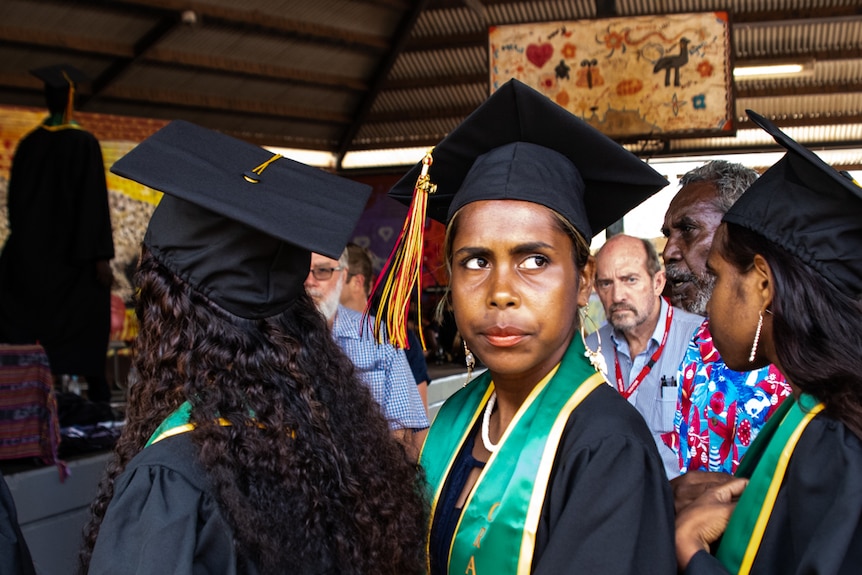 A woman stares off camera dressed in a graduation gown.