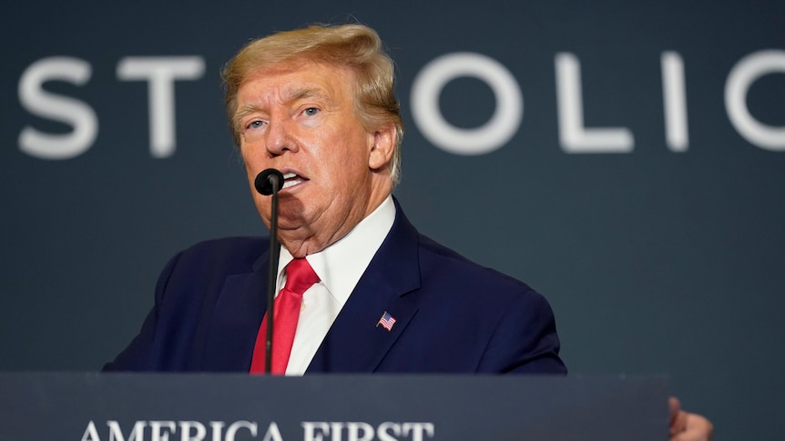 Donald Trump stands in front of a podium addressing a policy summit.