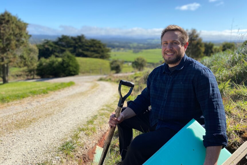 Jakob Sprickerhof from Landcare Tasmania stands on the farm with a shovel and tree guard.