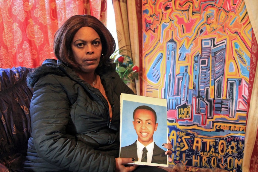 A woman sitting on a couch holding a photograph of her missing son