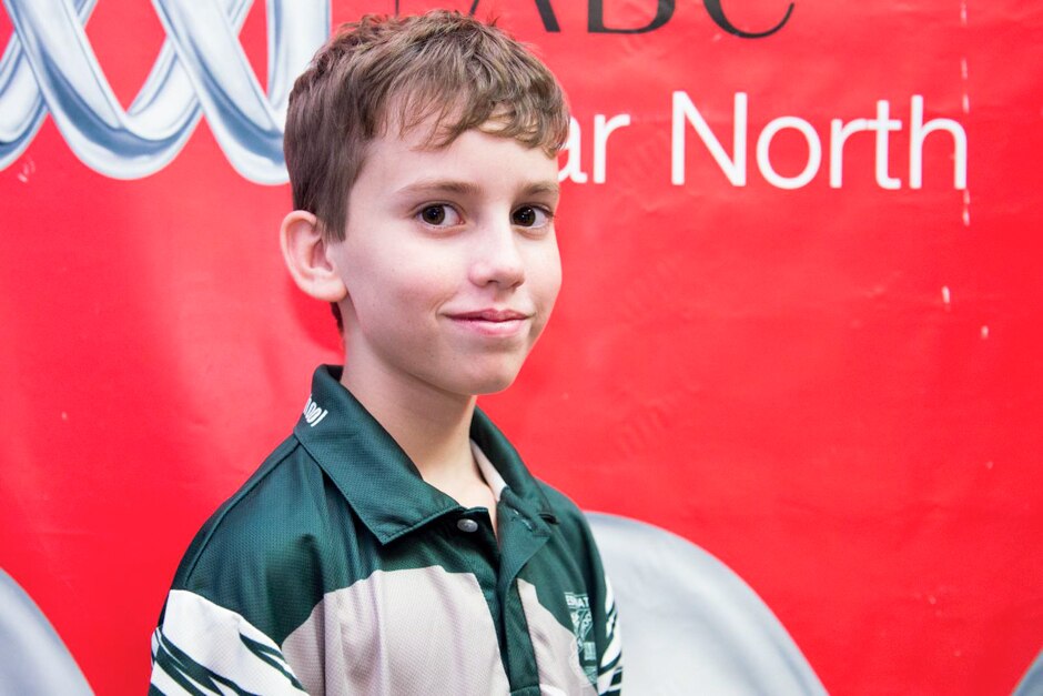 A year six boy stands in front of a bright red banner.