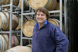 A man standing in front of wine barrels. 