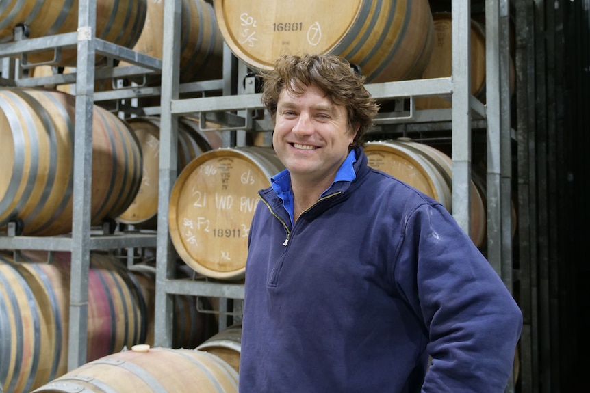 A man standing in front of wine barrels. 