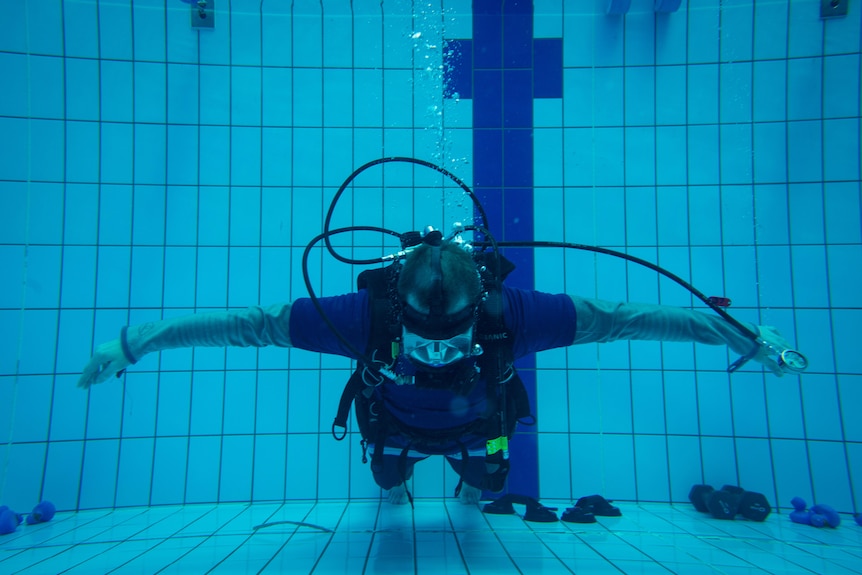 Man underwater in swimming pool wearing a scuba outfit and lifting weights