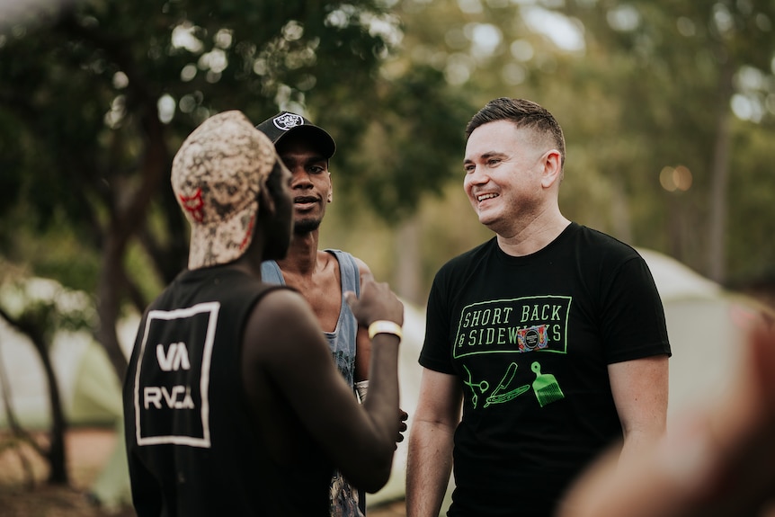 A smiling man speaks to two young men wearing baseball caps