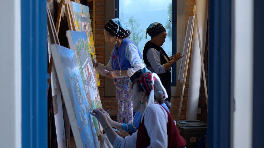 Colour still of four women, dressed in traditional Bai garb, painting on canvases in a room in 2018 documentary Up the Mountain.