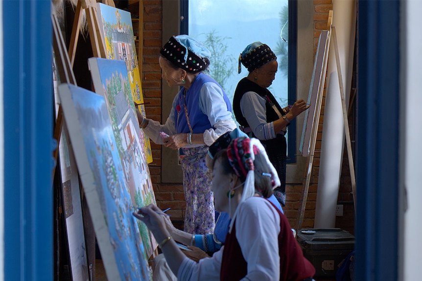 Colour still of four women, dressed in traditional Bai garb, painting on canvases in a room in 2018 documentary Up the Mountain.