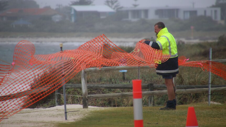 A worker secures a warning fence around collapsed dunes at a Lancelin beach.