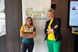 A woman and a teenage girl in green and gold smile with arms folded in front of a banner that says Green & Gold Athletes.