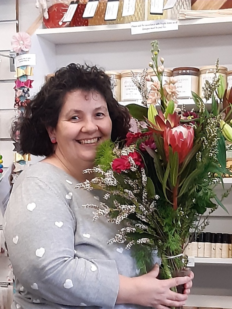 lady with curly brown hair holding bunch of brightly coloured flowers