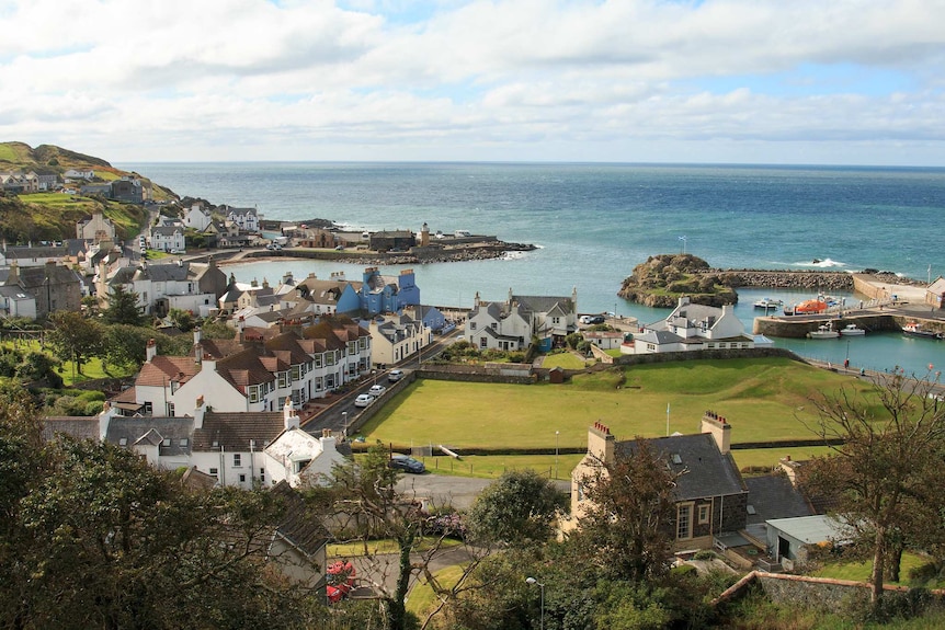 An idyllic British seaside village is shown from a high vantage point on a sunny day.