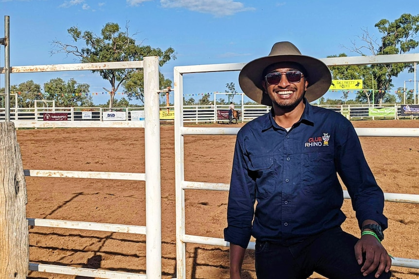 a young man in an akubra hat stands in front of a what looks like a rodeo arena