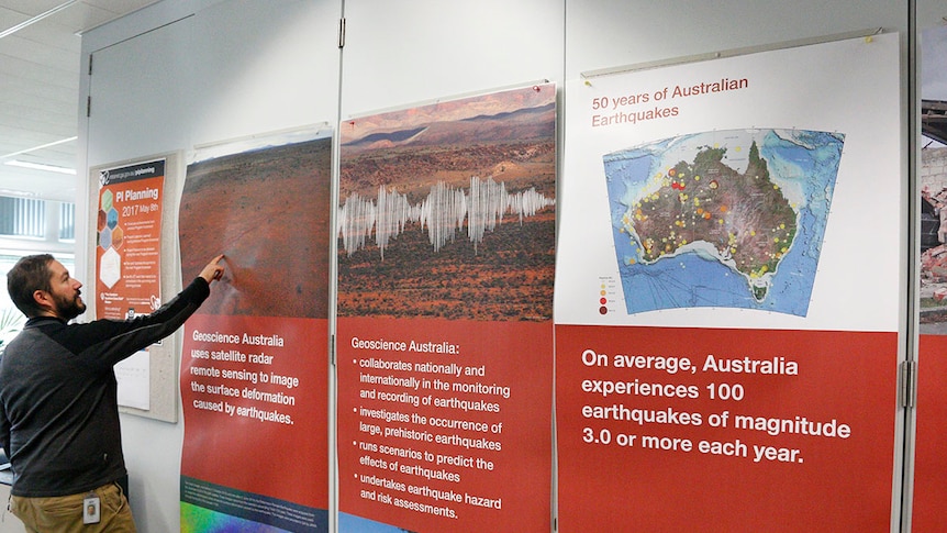 Man pointing to various fault lines on a large sign in the Geoscience Australia building.