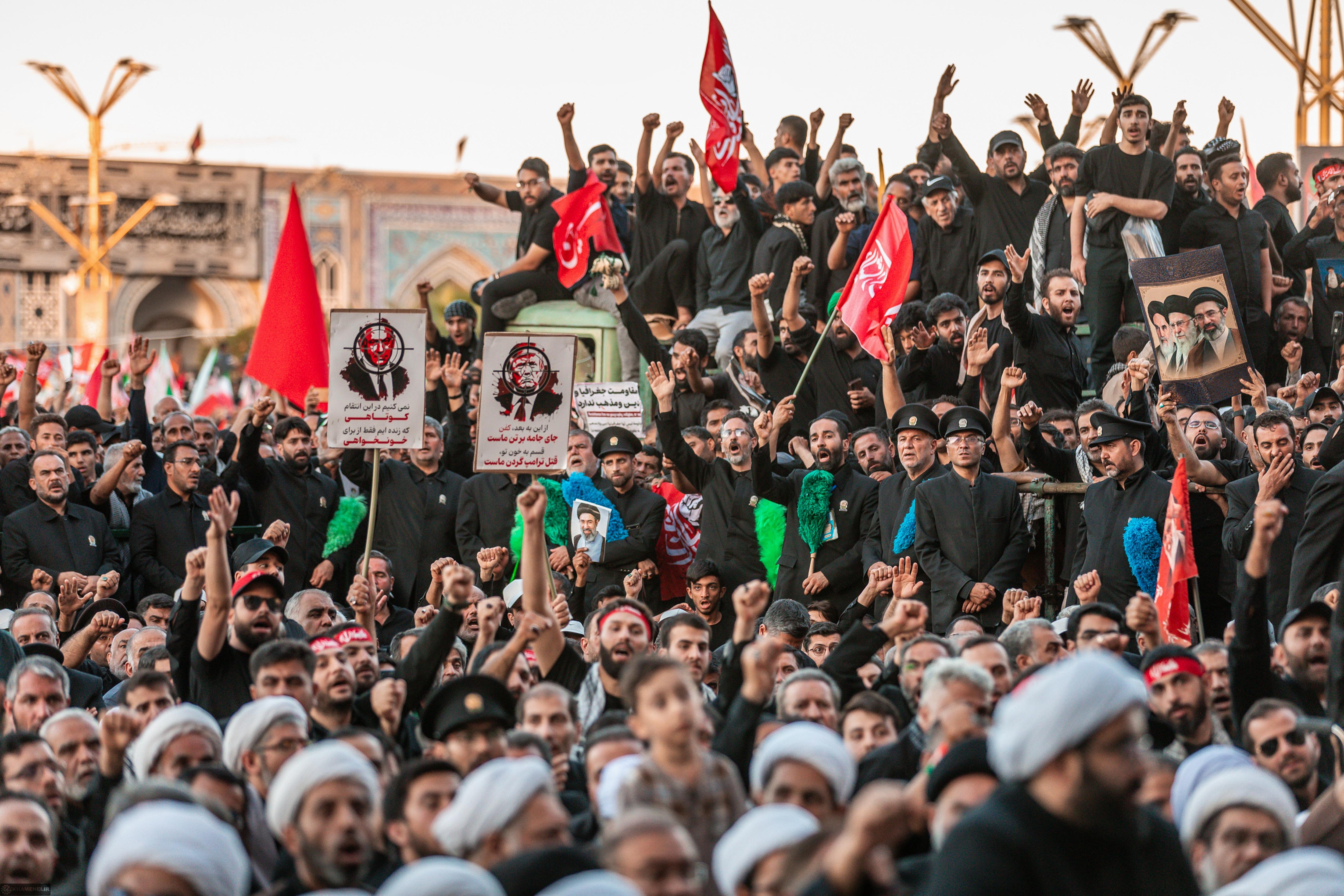 A large crowd dressed in black and holding red flags at a funeral ceremony. 