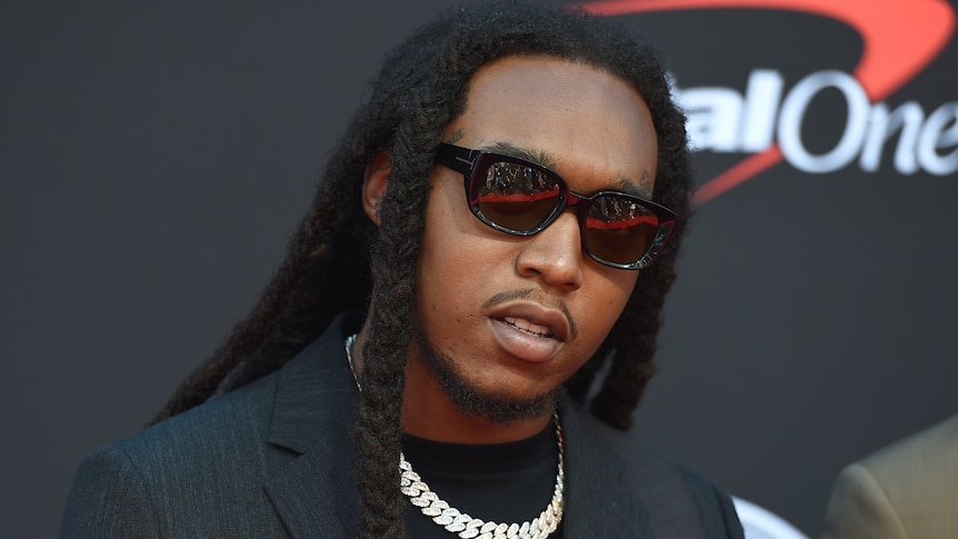 Takeoff stands on teh red carpet in sunglasses and a suit. 