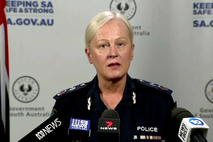 A blonde woman wearing a police uniform with microphones in front of her.