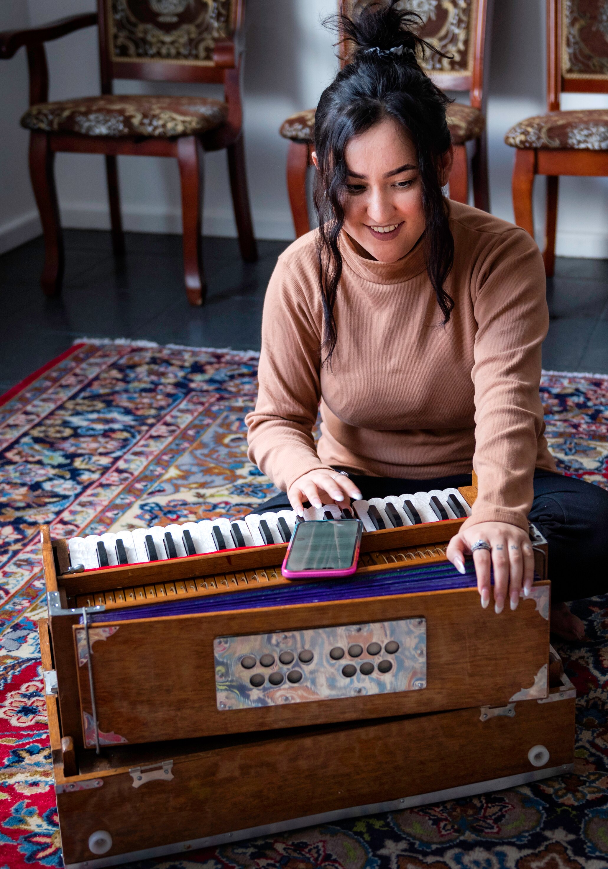 A young Afghan woman smiles brightly as she presses the keys of a harmonium