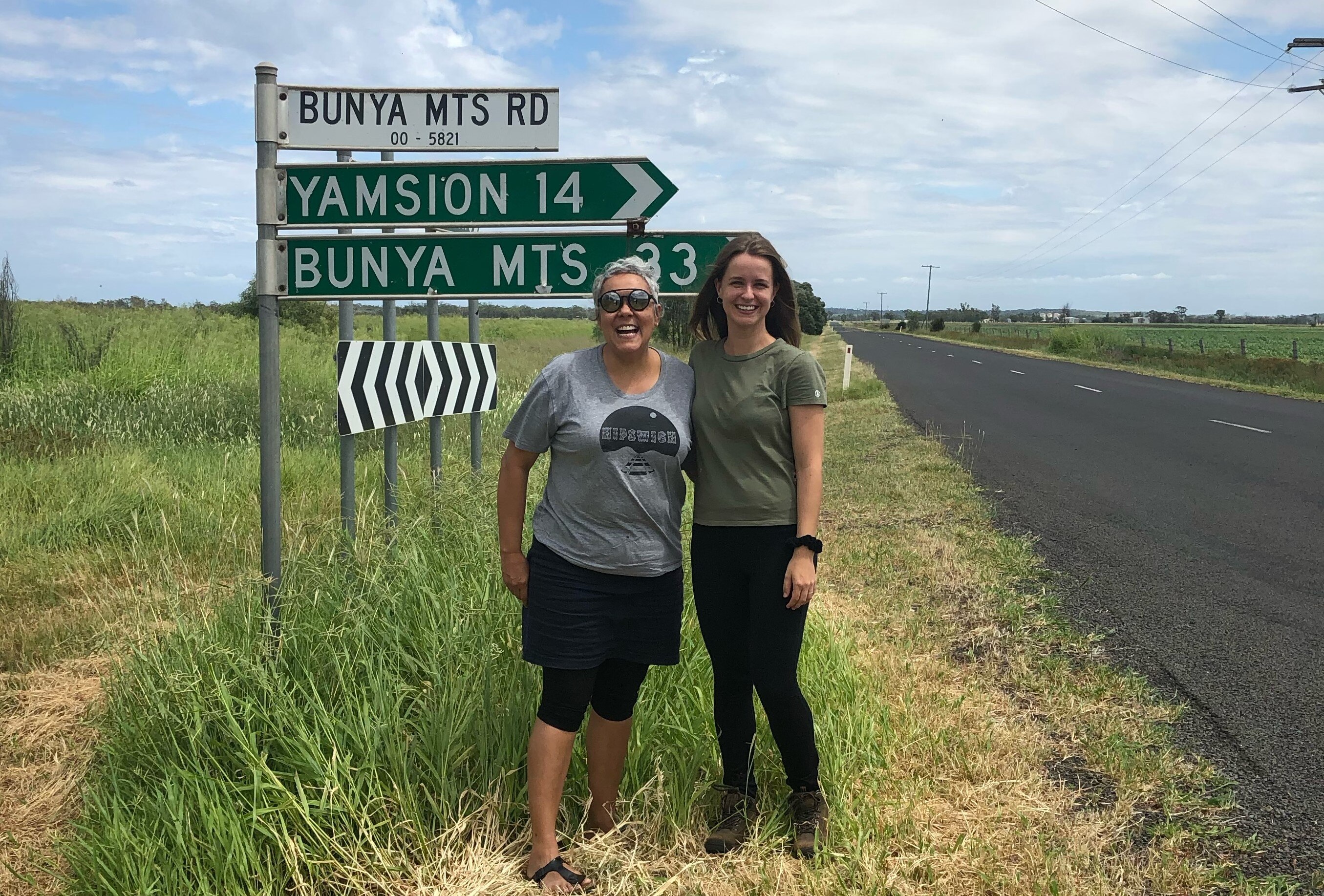 Two women standing next to a sign pointing to the Bunya Mountains.