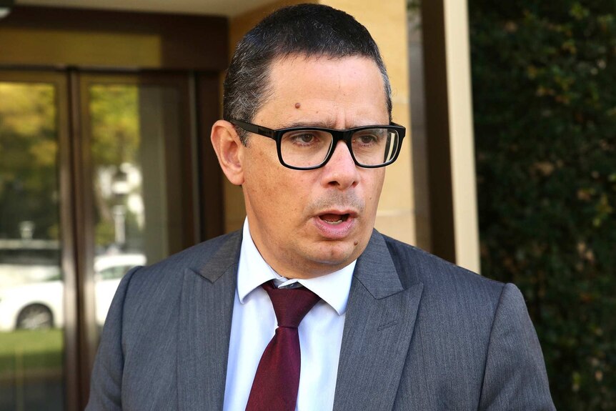 A head and shoulders shot of WA Treasurer Ben Wyatt wearing a grey suit, white shirt and red tie with spectacles on.
