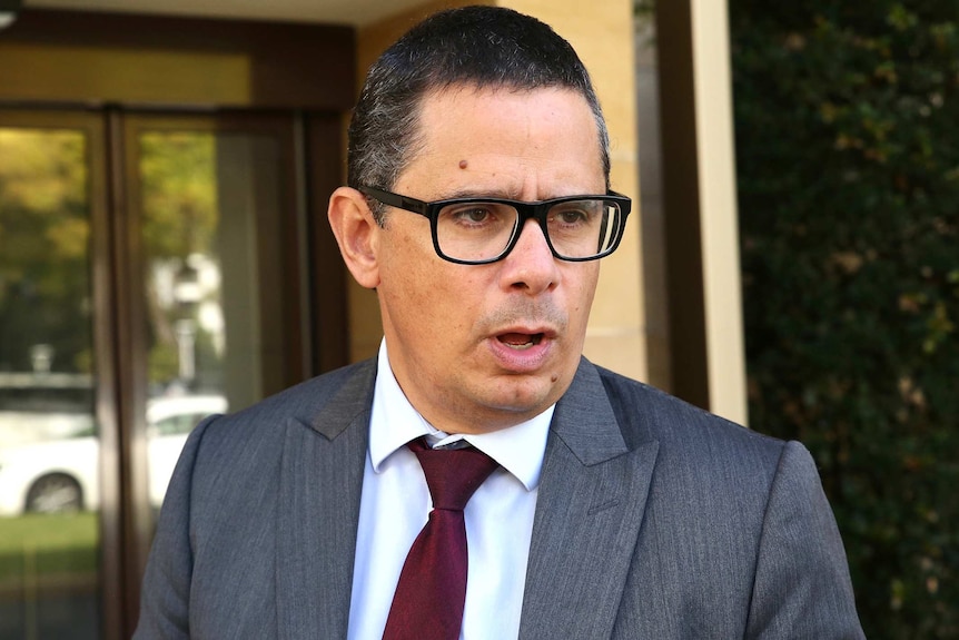 A head and shoulders shot of WA Treasurer Ben Wyatt wearing a grey suit, white shirt and red tie with spectacles on.