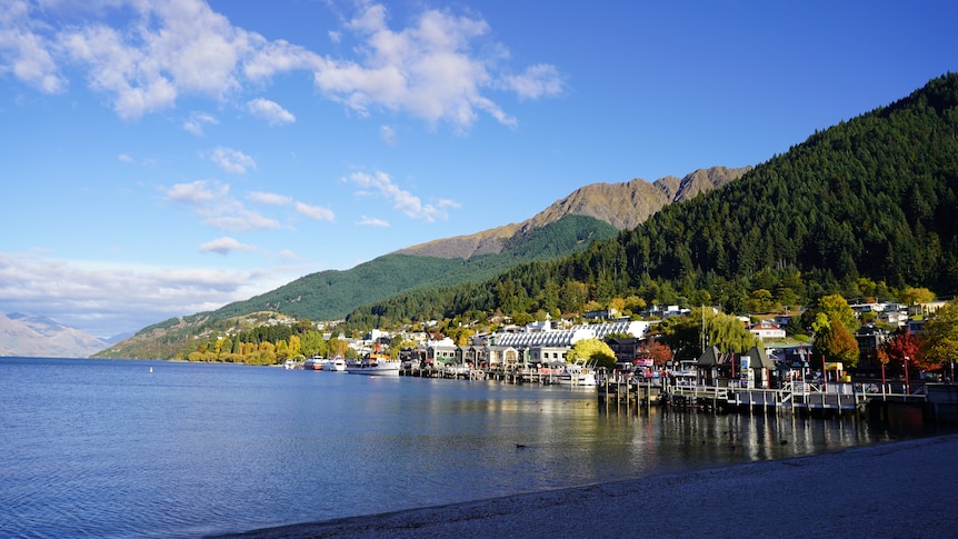 A landscape photo of a town residing between mountains and a lake with a blue sky above. 