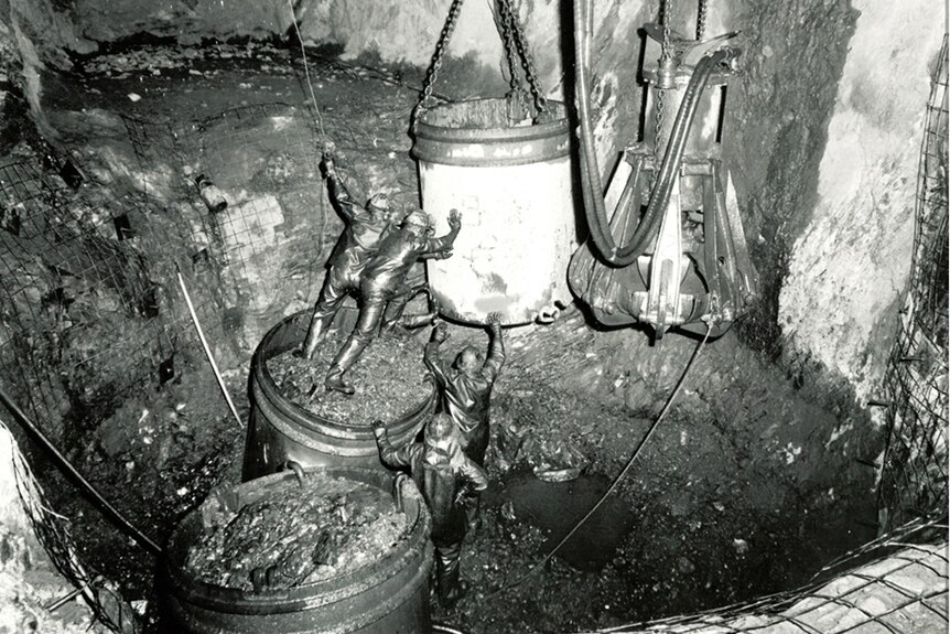 Miners covered in dirt hard at work in a shaft.