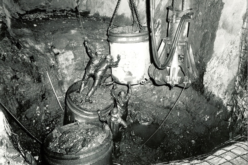 Mineros cubiertos de tierra trabajando duro en un pozo.