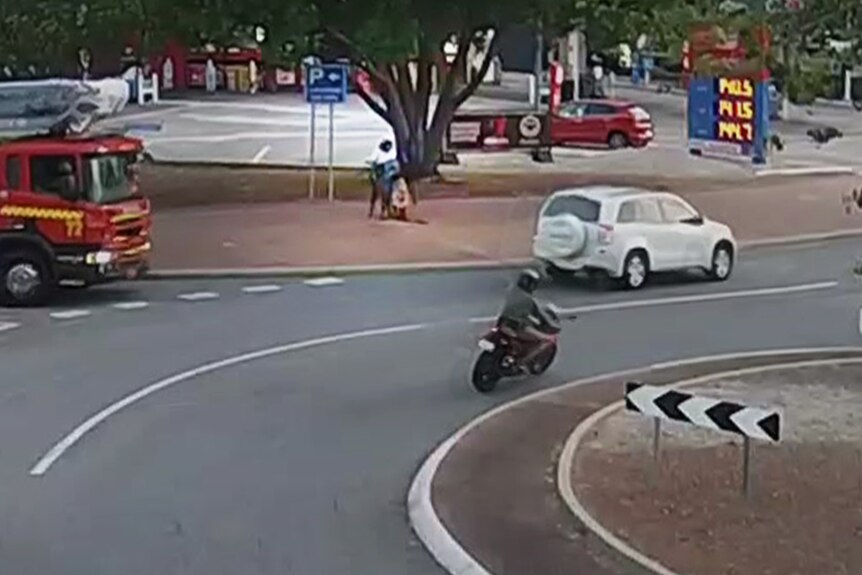 A busy roundabout in Darwin which shows a man holding a woman. Lots of cars drive past.