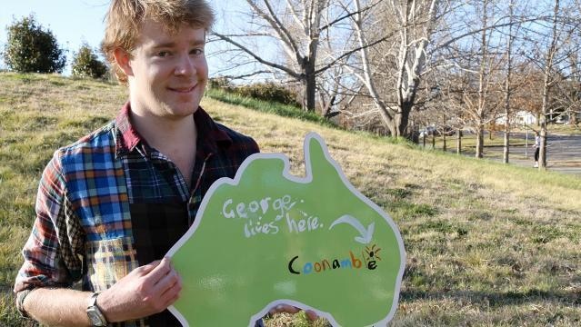 Teenage boy holds up sign in shape of Australia, text reads "George lives here", arrow points to "Coonamble"