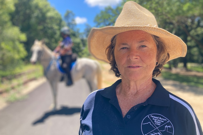 woman with short hair and a sun hat looking at camera with a horse in the background