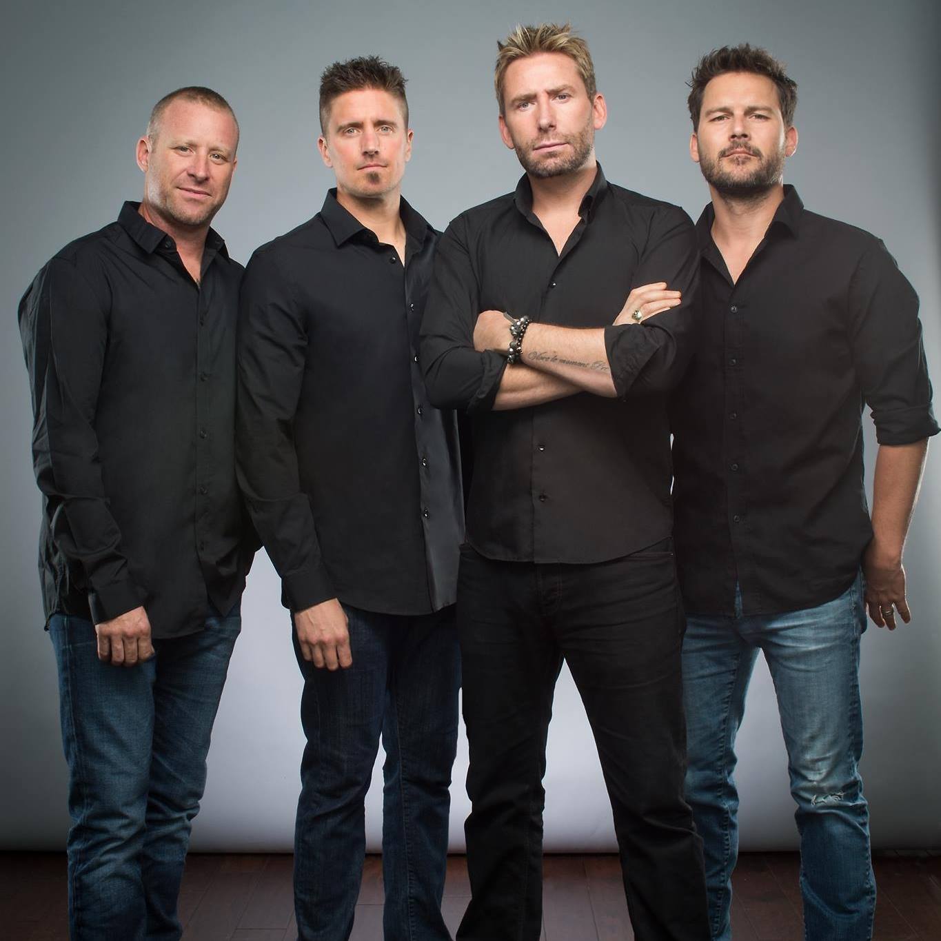four members of rock band nickelback stand side by side wearing black shirts and jeans 