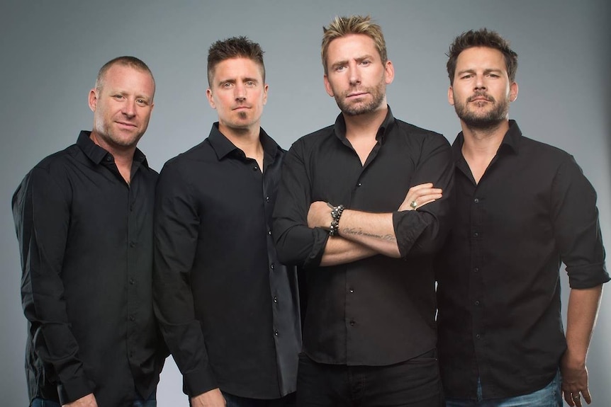 four members of rock band nickelback stand side by side wearing black shirts and jeans 