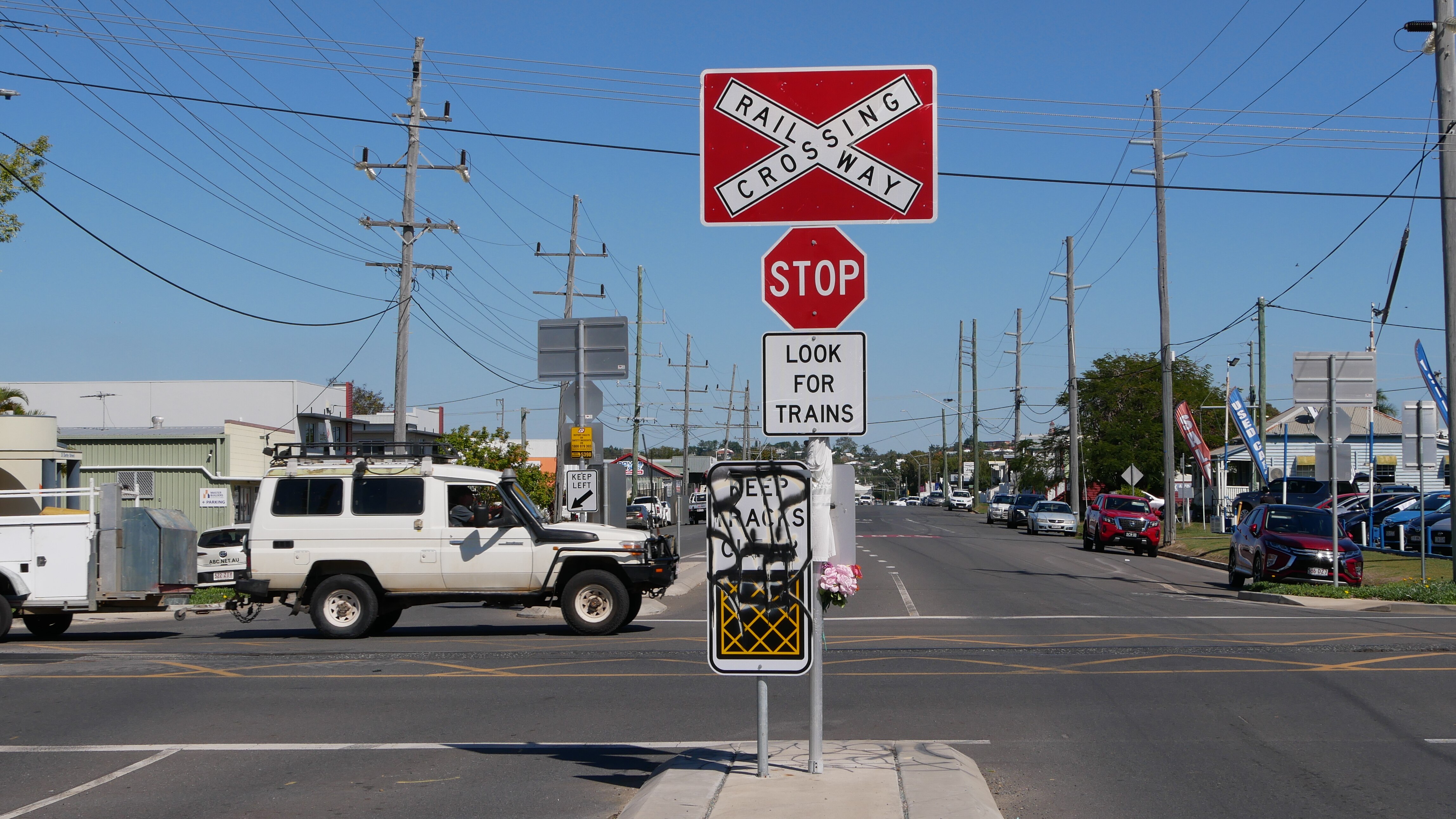 A car drives beside a rail line.  A stop sign and railway crossing crossing is in the center of the road.