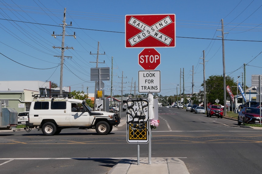A car drives beside a rail line. A stop sign and railway crossing crossing is in the centre of the road.