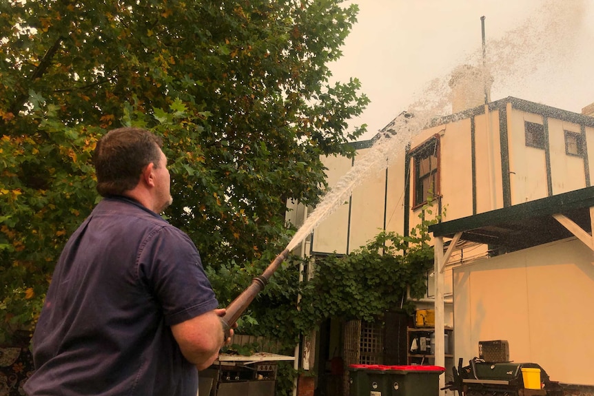 A man sprays water over the roof of a pub under an orange-tinged sky.