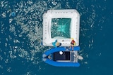 An aerial shot looking down over a small dinghy boat and a square floatation device