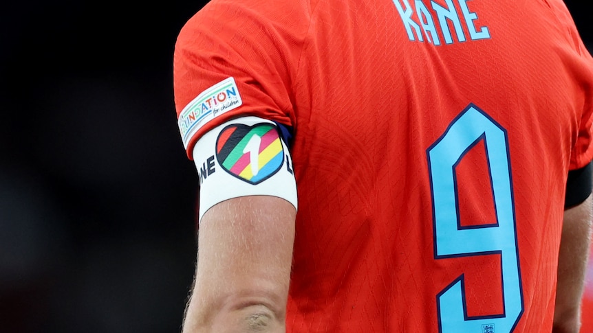 The back of a football player. His shirt is red with number 9 and 'Kane'. On his left arm an armband with a rainbow heart.