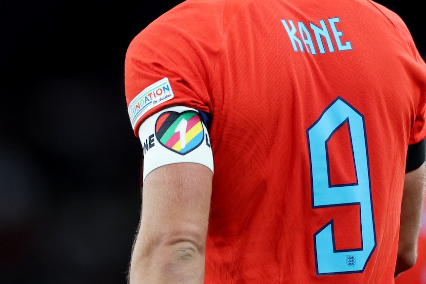 The back of a football player. His shirt is red with number 9 and 'Kane'. On his left arm an armband with a rainbow heart.