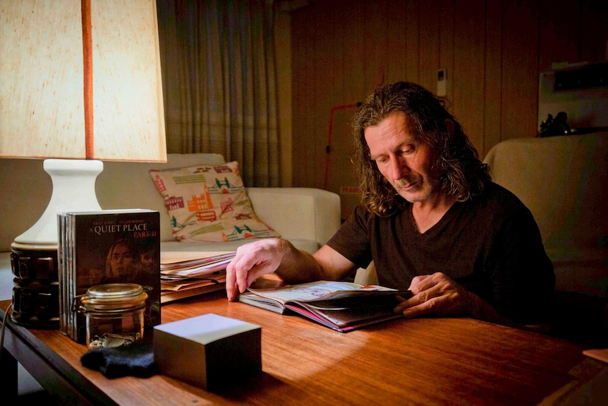 A middle-aged white man sitting in a dark room with a lamp on