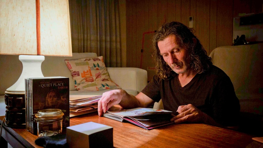 A middle-aged white man sitting in a dark room with a lamp on