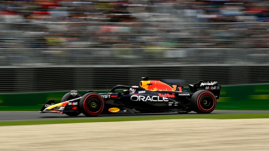 Max Verstappen in his Red BUll F1 car driving on track at Albert Park in Melbourne past a grandstand