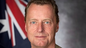A man in a uniform stands in front of an Australian flag.