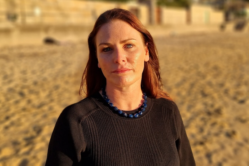 A woman wearing a black top stands on sand at a beach.