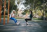 Two women wearing activewear sitting on swings, talking and laughing