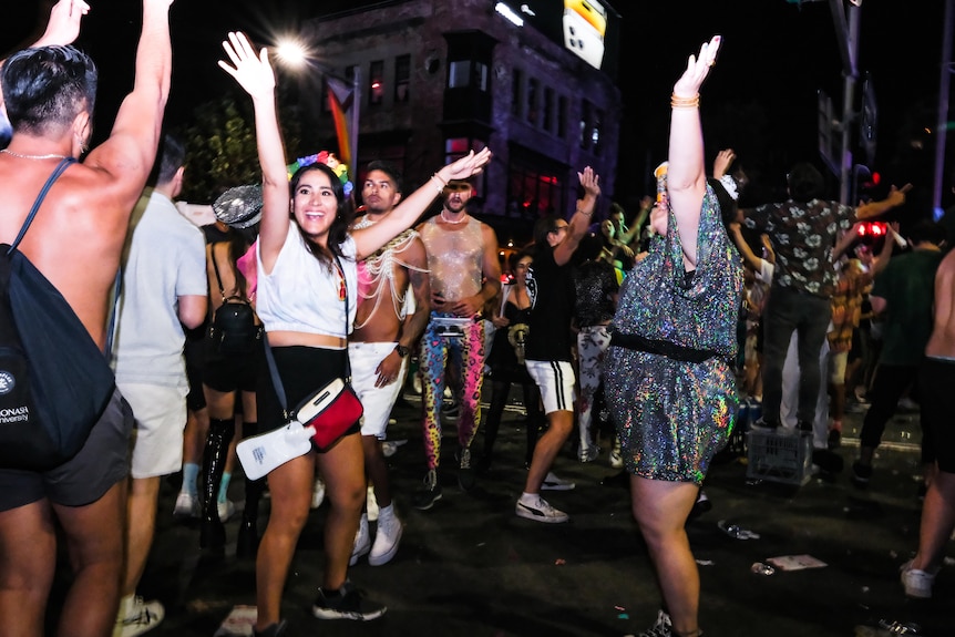 Les fêtards dans une rue tiennent leurs bras dans le ciel nocturne