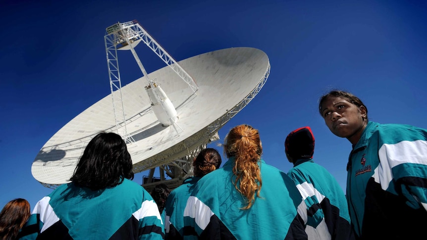 A group of Indigenous students cluster around a satellite dish.