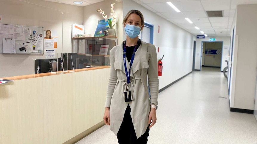 A woman in a blue face mask stands in a hospital corridor, in a story on end-of-life care during COVID pandemic.