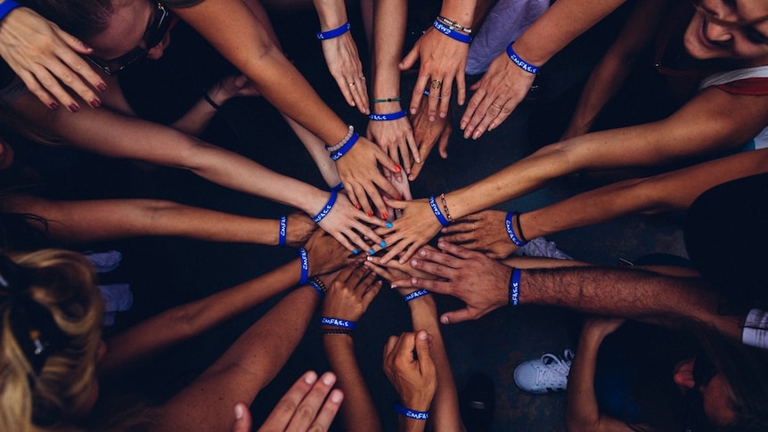 A group of people with different skin tones with their hands together in a circle shown from above.