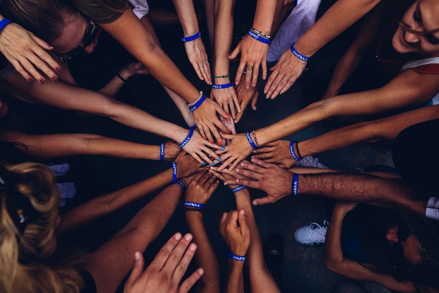 A group of people with different skin tones with their hands together in a circle shown from above.